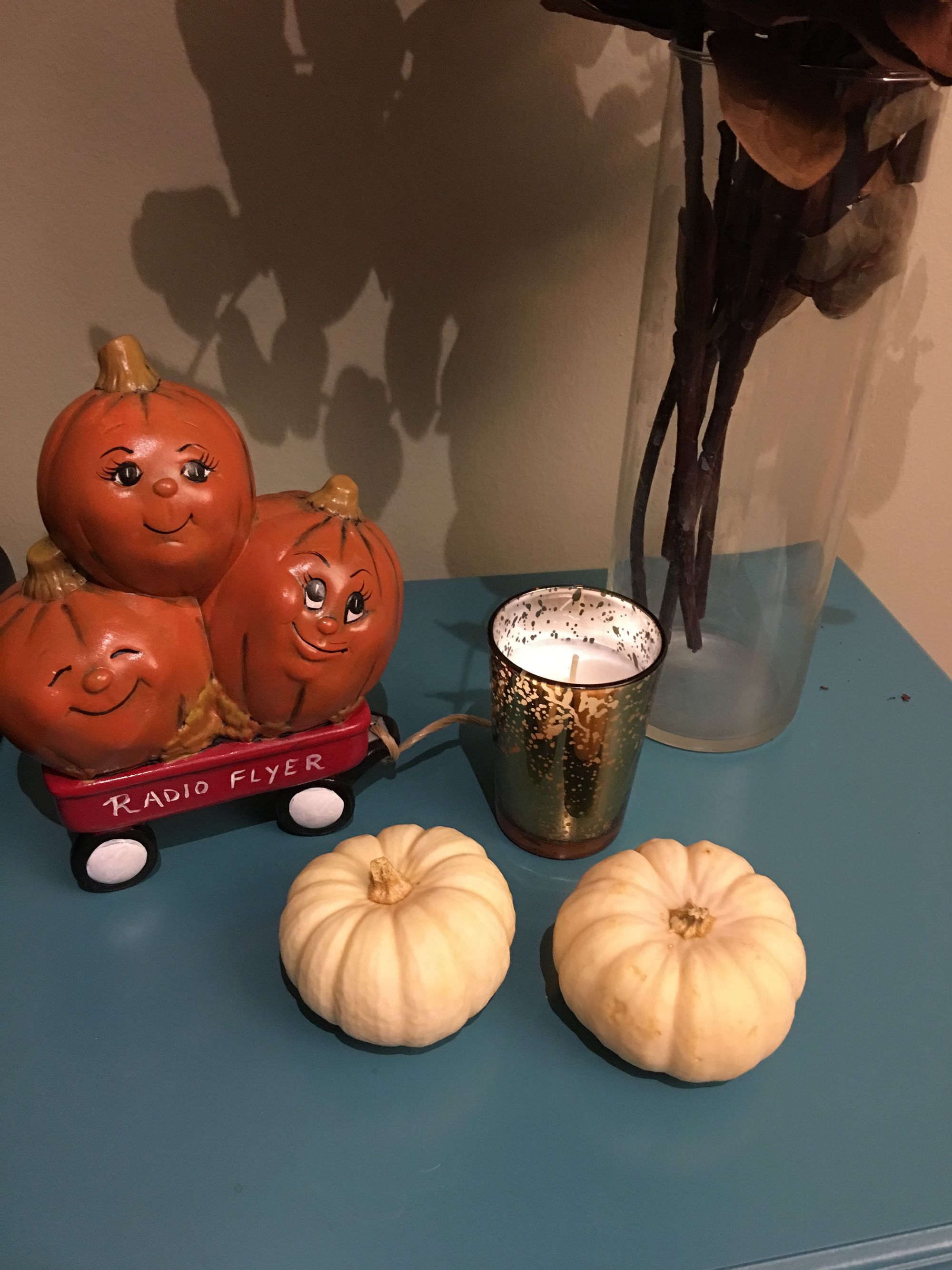 A ceramic Radio Flyer wagon with three pumpkins and two small white pumpkins sitting nearby