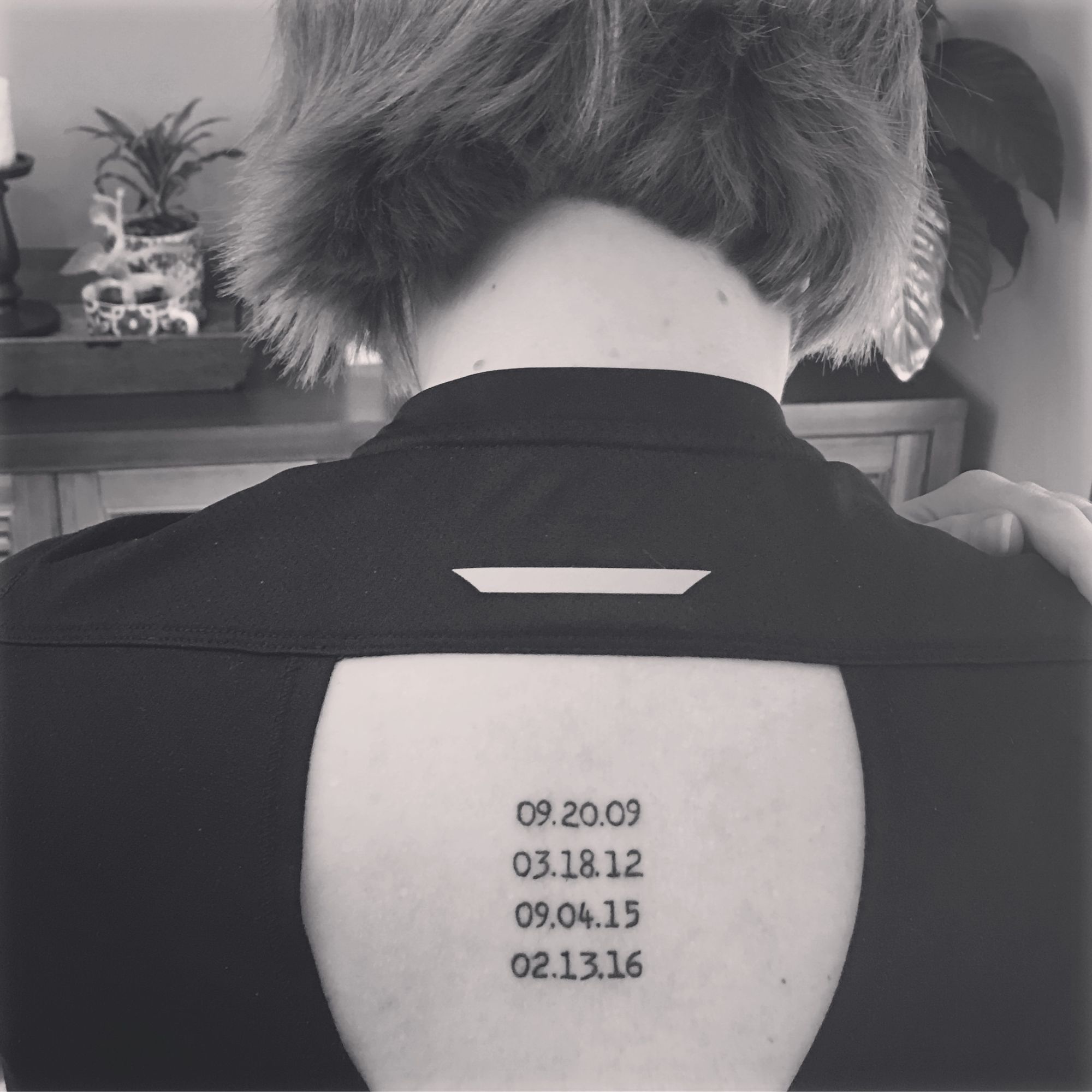 Black and white image of a woman's back, showing a tattoo of four dates in a typewriter font