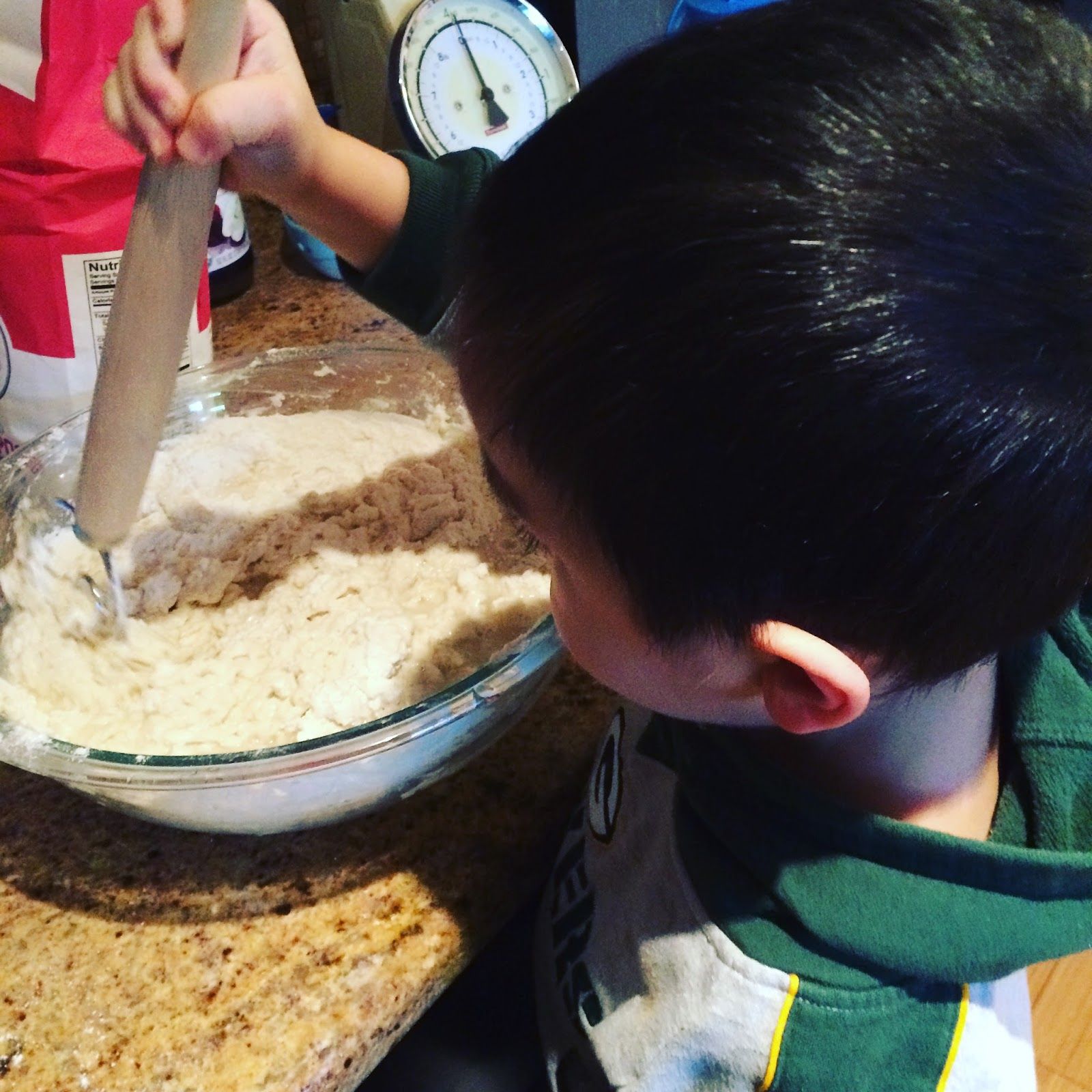 A small child with black hair mixing dough